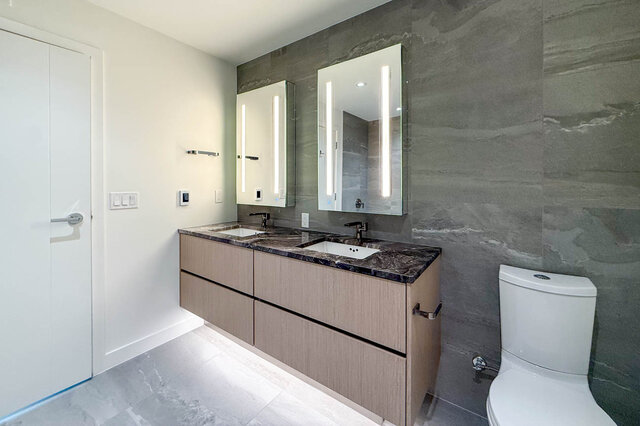 Modern bathroom with dark marble countertops and light wood cabinets. - 406-777 Harbour Way, North Vancouver