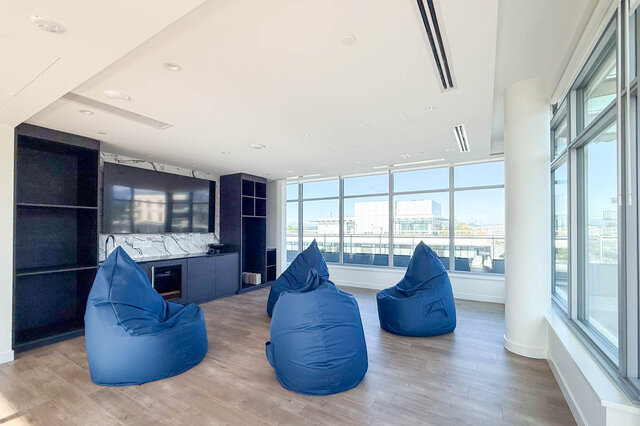 The lounge features blue bean bags, a TV, hardwood floors, and floor-to-ceiling windows with a city view. - 406-777 Harbour Way, North Vancouver