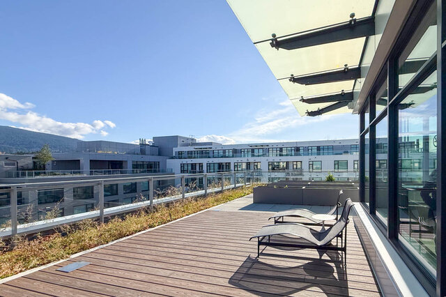 The balcony has a wooden deck, lounge chairs, a railing, and a view of mountains and buildings. - 406-777 Harbour Way, North Vancouver