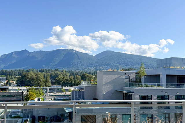 The balcony features a railing with a view of city buildings, trees, and mountains under a blue sky. - 406-777 Harbour Way, North Vancouver