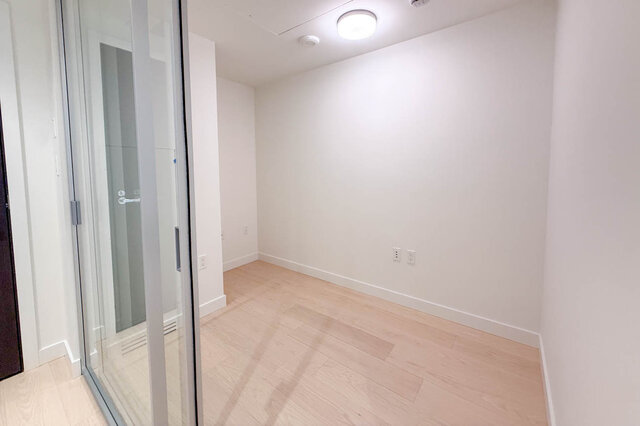 The room is an empty space with light wood flooring, white walls, a ceiling light, and electrical outlets. - 406-777 Harbour Way, North Vancouver