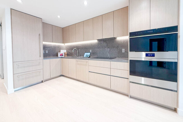 The kitchen has light wood cabinets, a stainless steel oven, under-cabinet lighting, and gray countertops. - 406-777 Harbour Way, North Vancouver