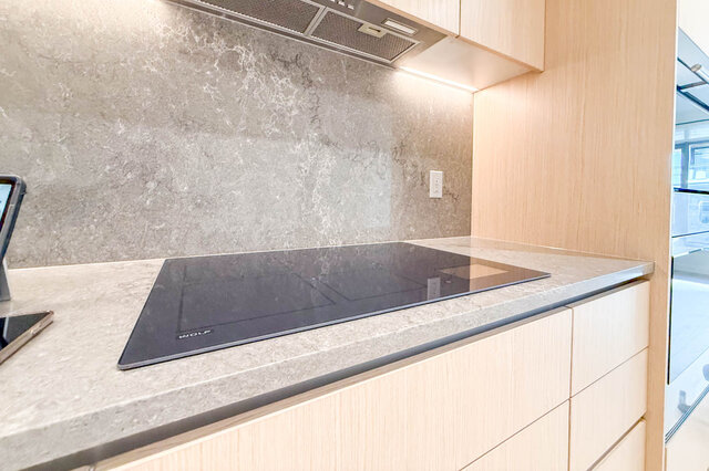 The kitchen features a light wood cabinet, stone backsplash, stainless steel cooktop, and range hood. - 406-777 Harbour Way, North Vancouver