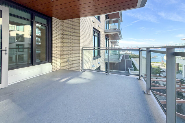 The balcony features a concrete floor, glass railing, and a view of water and distant buildings. - 406-777 Harbour Way, North Vancouver