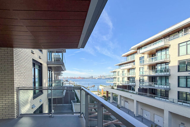 The balcony features a glass railing and overlooks a body of water with a city skyline in the distance. - 406-777 Harbour Way, North Vancouver