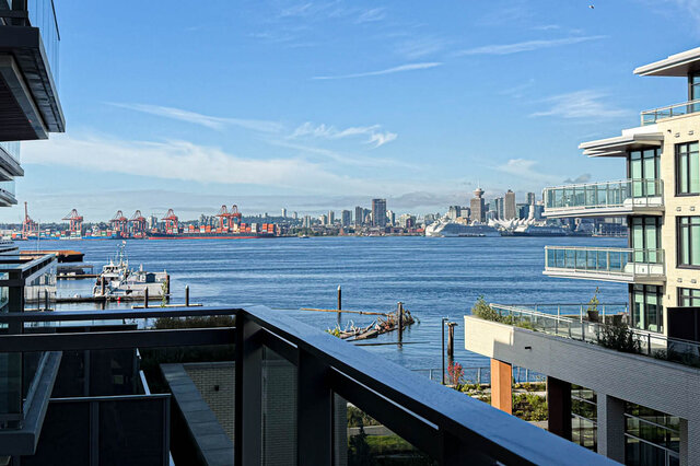 The balcony features a railing and a view of the water, city skyline, and port cranes. - 406-777 Harbour Way, North Vancouver