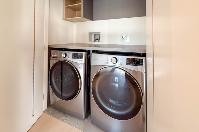 Laundry room with two stainless steel appliances, a countertop, and a cabinet. - 406-777 Harbour Way, North Vancouver