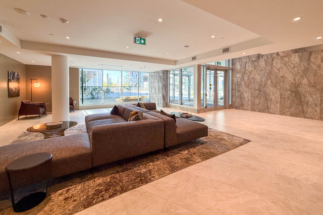 The lobby features a large sectional sofa, floor-to-ceiling windows, a marble wall, and recessed ceiling lighting.
