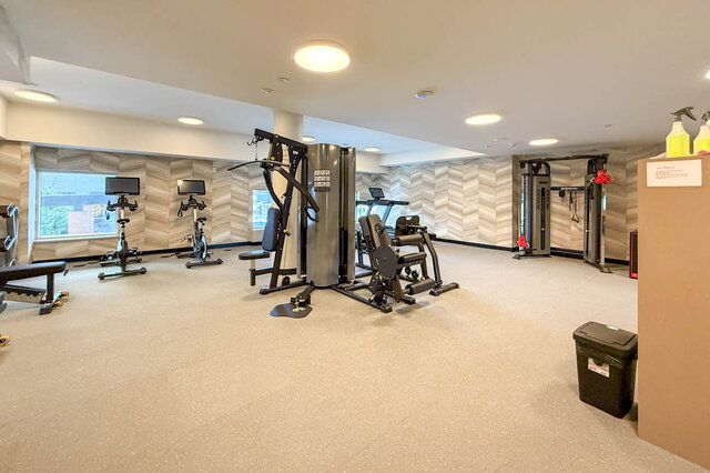The gym contains various exercise machines, large windows, and a carpeted floor. - 406-777 Harbour Way, North Vancouver