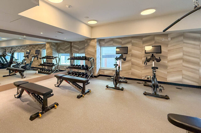 The gym features weight benches, dumbbell racks, indoor cycling bikes, and full-length mirrors. - 406-777 Harbour Way, North Vancouver