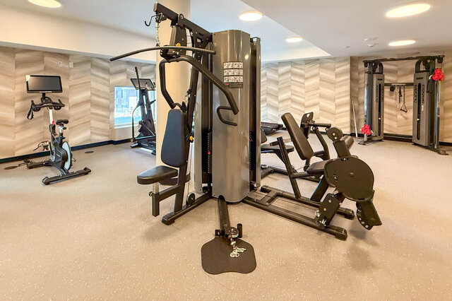 The gym features various exercise machines, a stationary bike, and patterned wall panels. - 406-777 Harbour Way, North Vancouver