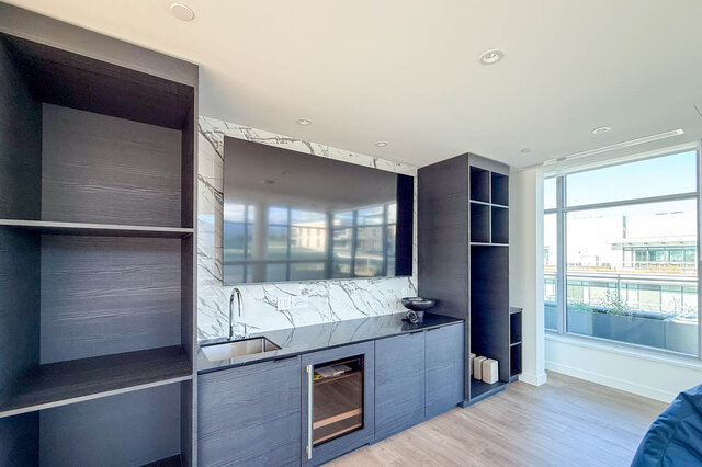 The living room features a large wall-mounted TV, built-in shelves, a countertop with a sink, and a wine cooler, with large w
