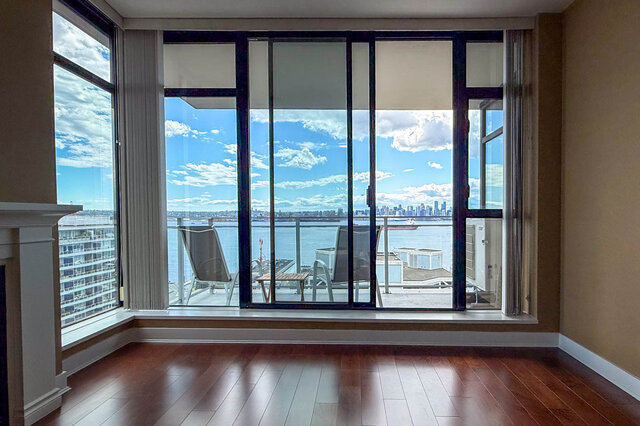 A living room with hardwood floors, a fireplace, and large windows overlooking a city skyline and water - 1601-155 1st Street West, North Vancouver