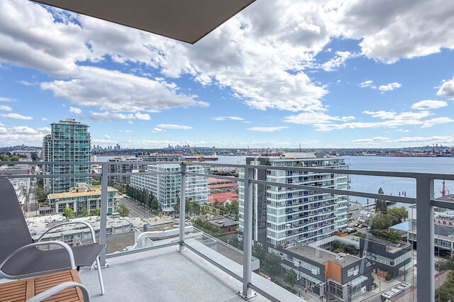 The balcony features outdoor seating and overlooks a cityscape with water. - 1601-155 1st Street West, North Vancouver