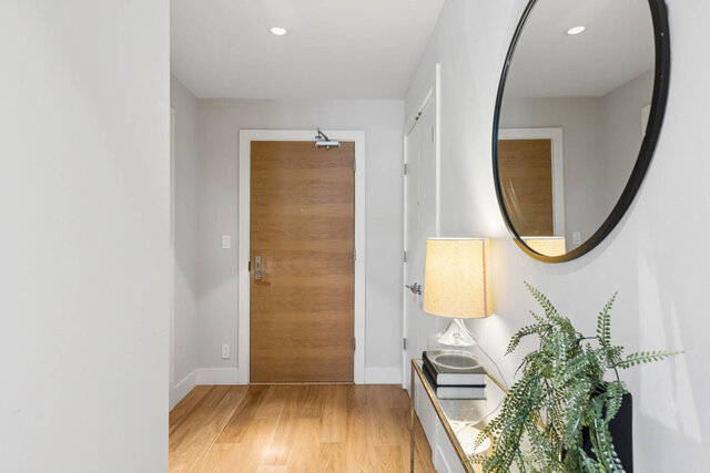 Entryway with light hardwood floors, large round mirror, and modern lamp. - 204-866 Arthur Erickson Place, West Vancouver