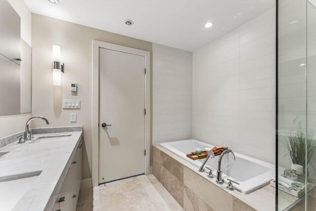 Modern bathroom with marble countertops and a built-in white tile tub. - 204-866 Arthur Erickson Place, West Vancouver