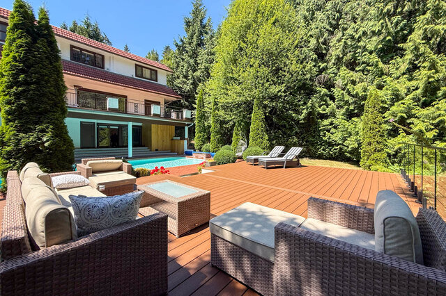 A sunny outdoor deck area with a pool, lounge furniture, and lush greenery surrounding a two-story house - 1249 Chartwell Place, West Vancouver