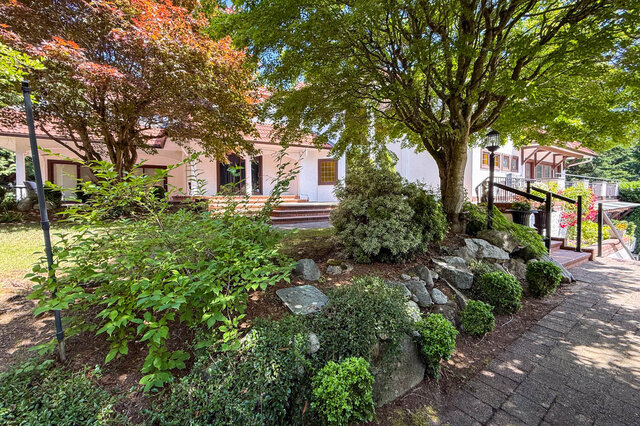 Sunny exterior view of a house with landscaped garden, stone pathway, and mature trees. - 1249 Chartwell Place, West Vancouver
