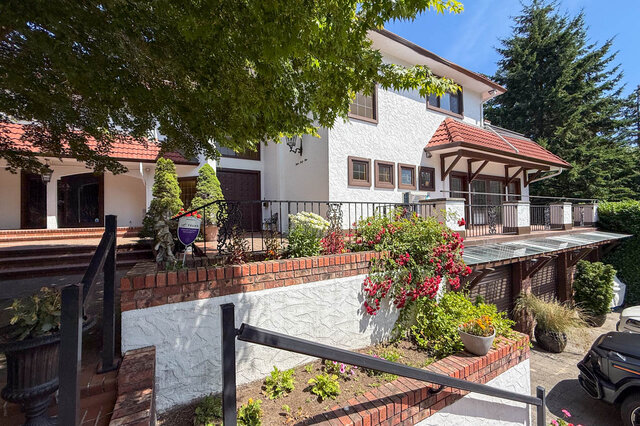 Exterior view of a white stucco house with red tile roof, brick accents, and lush garden landscaping - 1249 Chartwell Place, West Vancouver