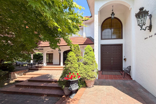 Bright exterior view of a house entrance with arched window, tiled patio, and landscaped garden - 1249 Chartwell Place, West Vancouver