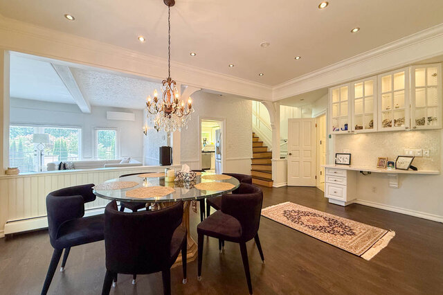 A well-lit dining area with a glass-top table, dark chairs, and a chandelier, showcasing hardwood floors and built-in cabinet