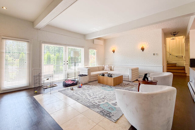 A bright living room with large windows, hardwood floors, and a dog crate. - 1249 Chartwell Place, West Vancouver