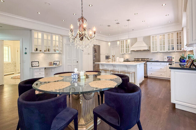 Bright dining area with glass-top table and blue velvet chairs, adjacent to a white kitchen - 1249 Chartwell Place, West Vancouver