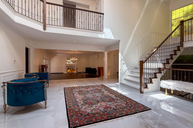 A spacious living room with a grand staircase, marble flooring, and a fireplace. - 1249 Chartwell Place, West Vancouver