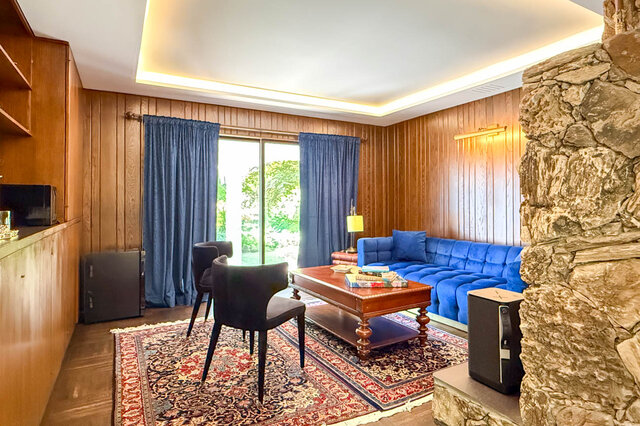Cozy living room with stone fireplace, blue velvet sofa, and large windows overlooking greenery - 1249 Chartwell Place, West Vancouver
