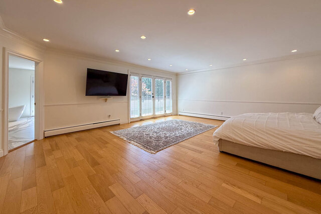 Spacious bedroom with hardwood floors, flat-screen TV, and large sliding glass doors - 1249 Chartwell Place, West Vancouver