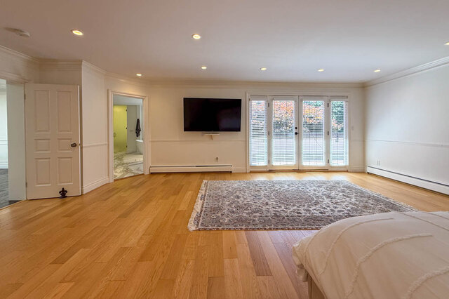 Spacious bedroom with hardwood floors, flat-screen TV, and French doors leading to an outdoor area - 1249 Chartwell Place, West Vancouver