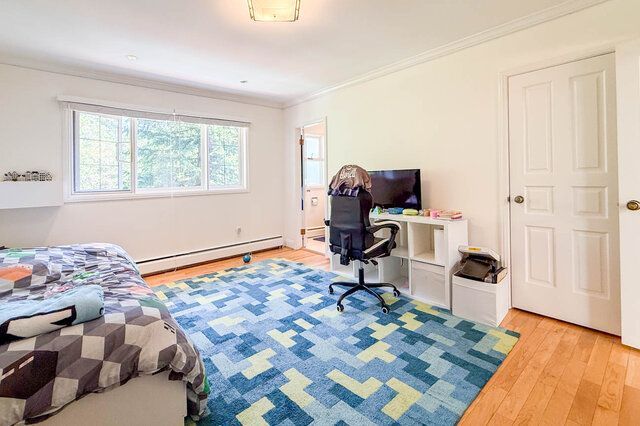 A bright bedroom with hardwood floors, large windows, and a colorful geometric rug. - 1249 Chartwell Place, West Vancouver