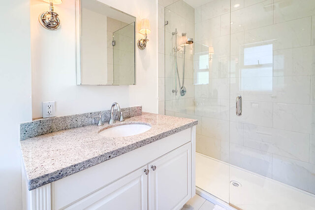 A bright, modern bathroom with a granite countertop, large mirror, glass shower enclosure, and small windows - 1249 Chartwell Place, West Vancouver