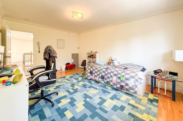 A bright bedroom with hardwood floors, a patterned bed, and a colorful rug - 1249 Chartwell Place, West Vancouver