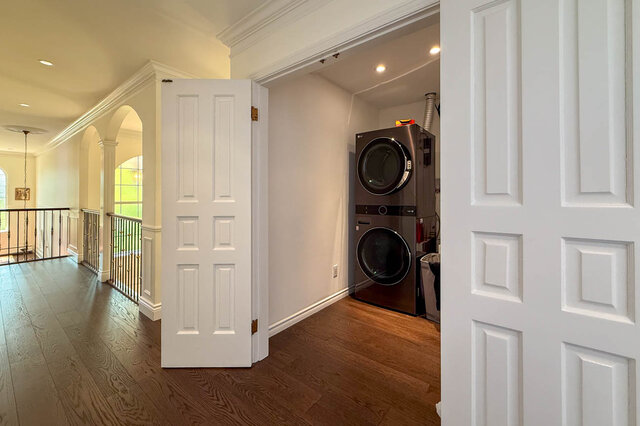A clean laundry room with stacked stainless washer and dryer and hardwood floors. - 1249 Chartwell Place, West Vancouver