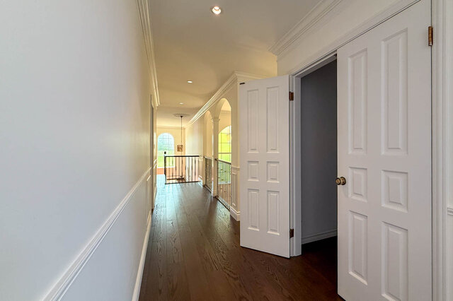 A well-lit hallway with hardwood floors, white panel doors, and a balcony view. - 1249 Chartwell Place, West Vancouver