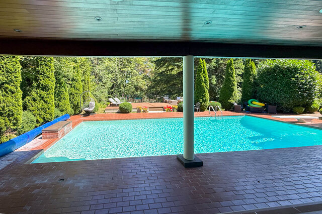 A bright exterior shot of a covered pool area with a clear blue pool, brick patio, and lush green landscaping - 1249 Chartwell Place, West Vancouver