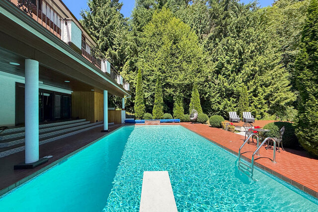A sunny exterior shot of a luxurious home with a clear blue pool, brick patio, and lush greenery. - 1249 Chartwell Place, West Vancouver