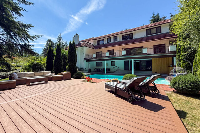 Exterior view of a multi-story building with a pool, wooden deck, and outdoor lounge chairs surrounded by greenery.