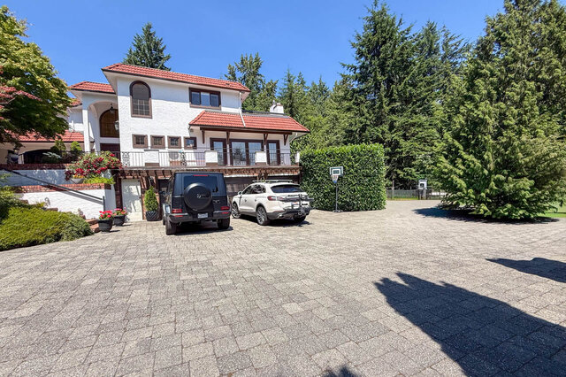 Exterior view of a white stucco house with red tile roof, paved driveway, and surrounding greenery - 1249 Chartwell Place, West Vancouver