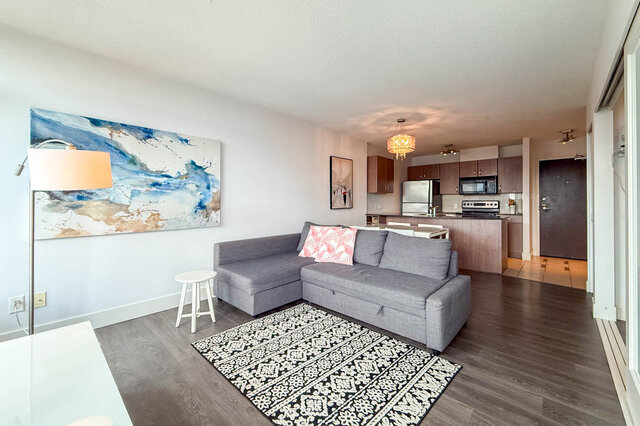 Living room with gray sectional sofa and hardwood floors near open-concept kitchen. - 2113-610 Granville Street, Vancouver Downtown