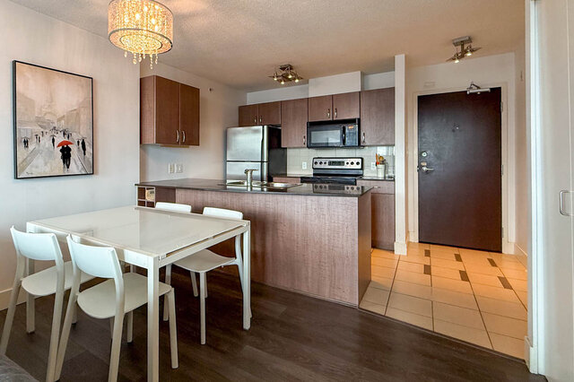 Bright kitchen and dining area with sleek dark countertops and modern white chairs on rich hardwood floors.