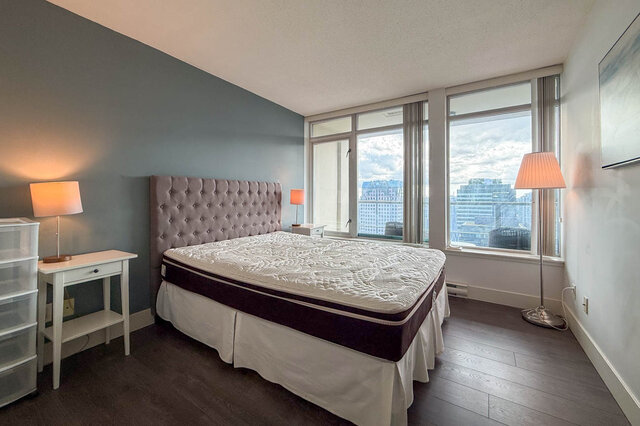 Spacious bedroom with tufted headboard, city skyline view, and dark hardwood floors. - 2113-610 Granville Street, Vancouver Downtown