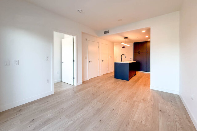 Spacious living area with light wood hardwood floors and blue kitchen island. - 204-1680 East 12th Avenue, Vancouver East Side