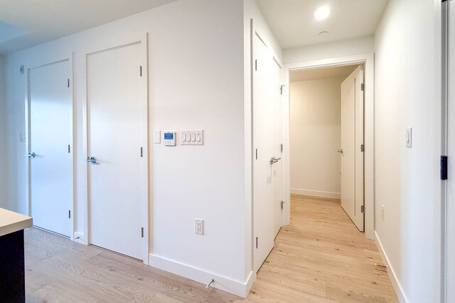 Bright hallway with light wood flooring and white doors, adjacent to kitchen counter. - 204-1680 East 12th Avenue, Vancouver East Side