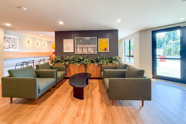 Cozy lounge with green sofas, wooden floors, and large windows overlooking the garden. - 204-1680 East 12th Avenue, Vancouver East Side