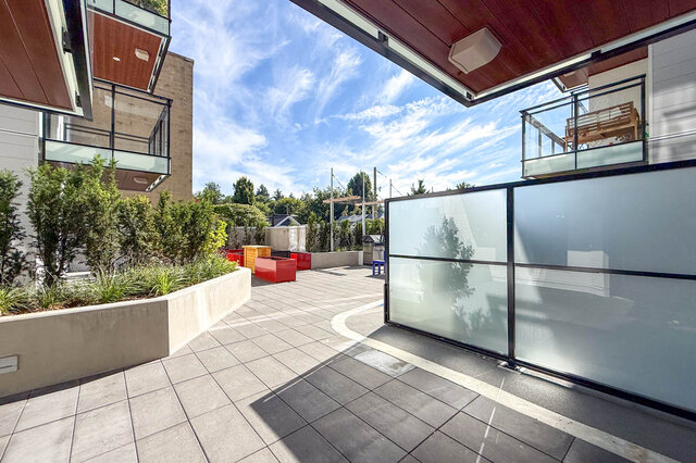 Modern patio with sleek glass walls and vibrant red seating. - 204-1680 East 12th Avenue, Vancouver East Side