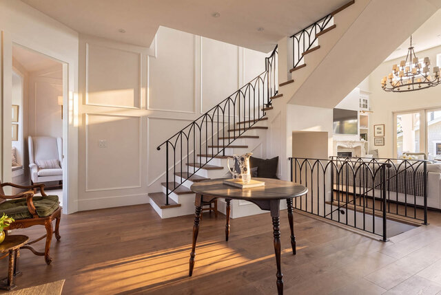 A bright living room with hardwood floors, wrought iron staircase, and large windows. - 1248 Kings Avenue, West Vancouver