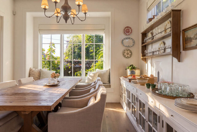 Bright dining area with a wooden table, chairs, large windows overlooking greenery, and built-in window seat - 1248 Kings Avenue, West Vancouver