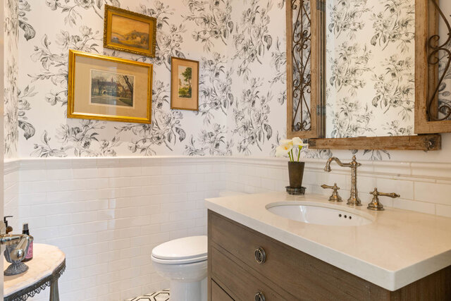 A stylish bathroom with floral wallpaper, white tile wainscoting, and a wooden vanity with brass fixtures. - 1248 Kings Avenue, West Vancouver